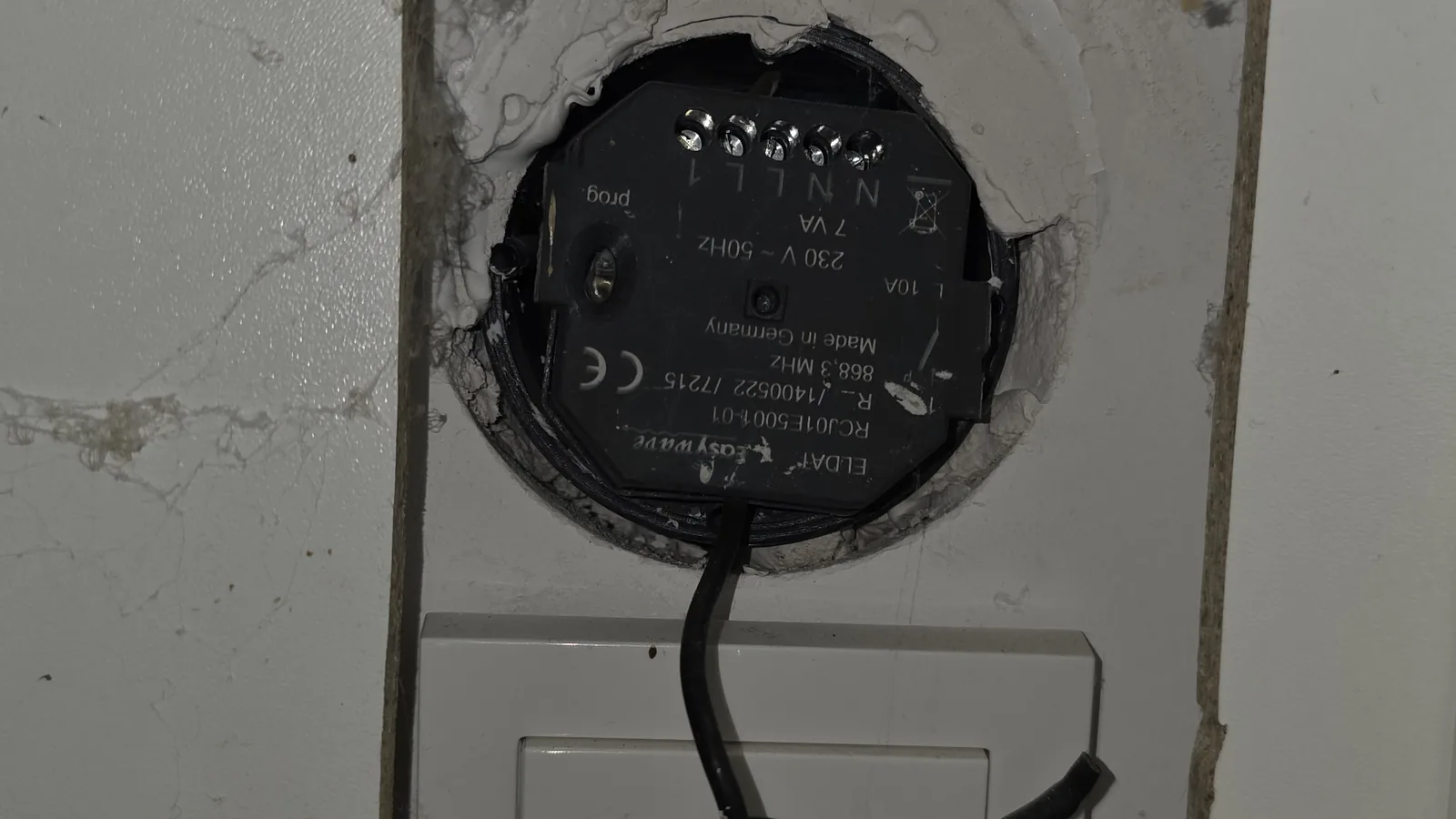 Funkempfänger ohne Gerätedose in einer Holzverkleidung, offene Schraubklemmen, daneben eine Steckdose mit geflicktem Kabel