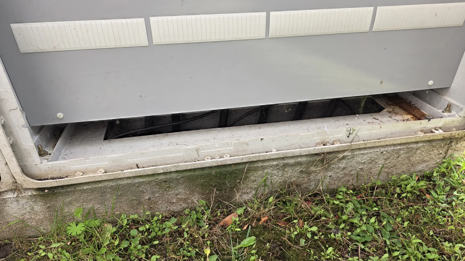 Offener Sockel einer Außen-Zähleranlage mit Rost am Rahmen, Moos und Erde am Übergang zum Beton