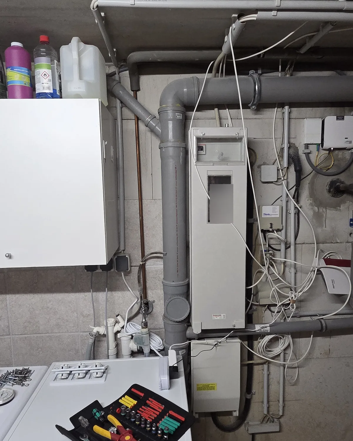 Waschkeller mit Zählerschrank zwischen Rohrleitungen, Datenleitungen ohne Kanal, Anschlussdosen und Router an der Wand