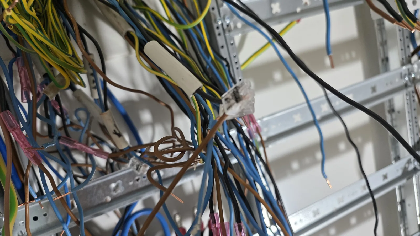 Alte Adern im geöffneten Zählerschrank: rosa Stoßverbinder, blanke Aderenden, Schlaufen, Beschriftung mit Klebeband